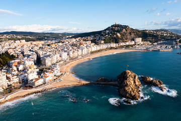Fototapeta premium Picturesque aerial view of Blanes cityscape on Mediterranean coast overlooking symbol of city, Sa Palomera Rock and San Juan hill with tower of medieval castle on sunny day, Catalonia, Spain..