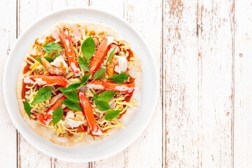 raw pizza with tomato sauce, shrimp, crab stick, sausage, sweet basil, oregano, mozzarella, cheddar, gouda, romano cheese in white ceramic plate on white wood texture background, top view, flat lay