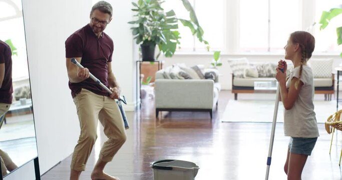 Rock out with your mop out. 4k video footage of a father singing and having fun while mopping the floor with his daughter at home.
