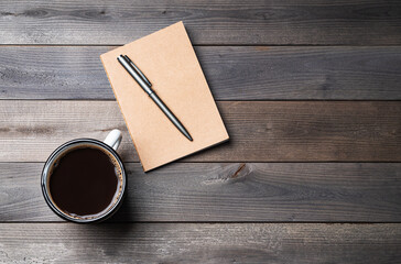 A cup of black coffee and craft notepad on a old wooden background. Concept of natural materials, travel planning, home and work office place. Top view  and copy space