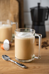 Two cups of freshly brewed aromatic coffee with milk on the kitchen table with a coffee pot and scattered grains. The concept of an early morning breakfast
