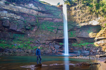 young man at waterfall falling streams from mountain top with reflection from different perspective