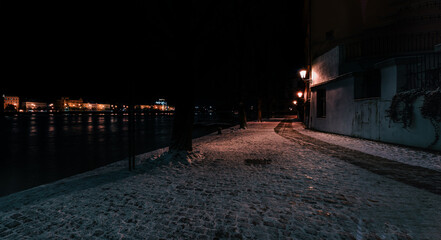 snowy sidewalk near Charles Bridge on Vltava river in Prague city center at night