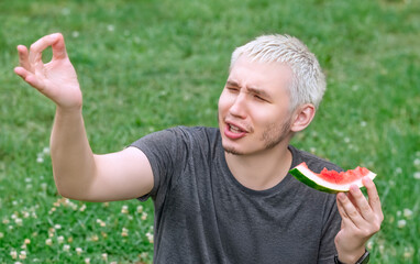 The guy is eating a watermelon sitting on the green lawn