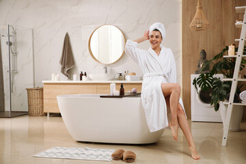 Beautiful young woman sitting on edge of tub in bathroom