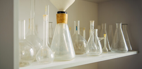 Various glass flasks on the shelf, close-up. Equipment for experiments in the school laboratory. Used empty test tubes.