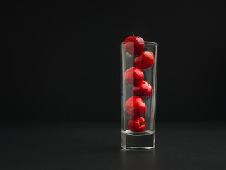 Ripe red acerola cherries in glass with a black background.