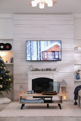 Stylish living room interior with modern TV, fireplace and Christmas tree
