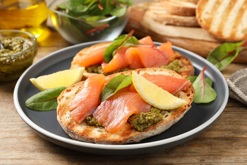 Delicious bruschettas with salmon and pesto sauce on wooden table, closeup