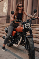Looking stylish woman posing on classic dark bike outdoors