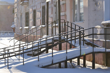 A snow-covered wheelchair ramp at the entrance to an apartment building. Winter cityscape.