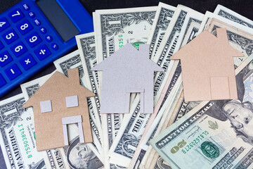 Brown paper house model with dollar banknotes and blue calculator
