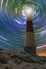 Amazing lighthouse in the hill of rock, star trail in the background at sunset