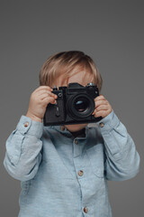 Cheerful child photographer with camera against gray background