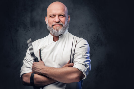 Bald elderly chef with kitchen spatula and tongs