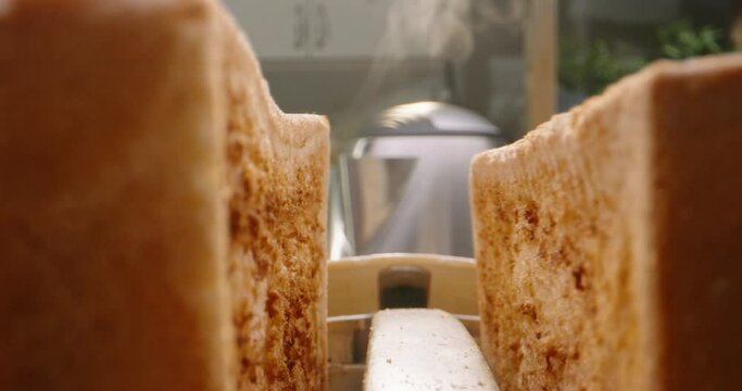 Close up shot of crunchy roasted bread jumping out of toaster with water steaming out of kettle on background - morning meal preparation, food and drink 4k footage