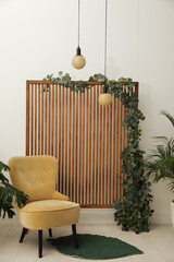 Stylish photo zone with wooden screen, floral decor and comfortable armchair indoors