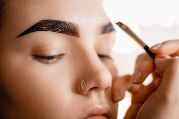 Correction and tint henna of eyebrows, master applies brush to woman marking on brow
