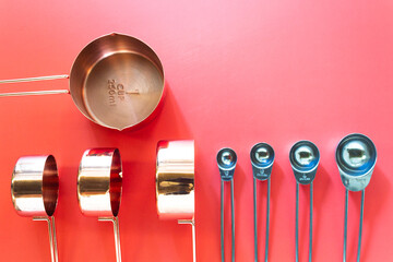 Collection of copper measuring cups and metal measuring spoons on red background in top view