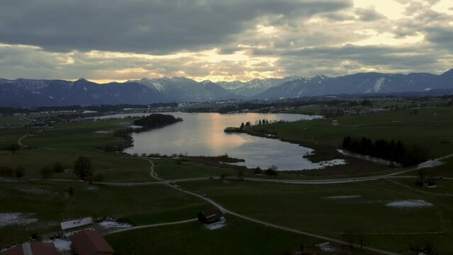 Scenic Bavarian lake Staffelsee in south Germany close to the alps with a  vibrant dramatic sunset cloud sky and idyllic mountains and green countryside fields. 4K UHD aerial drone footage