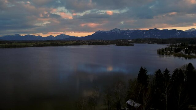 Beautiful lake Staffelsee in Bavarian in south Germany close to the alps and Munich with a  vibrant dramatic sunset cloud sky, idyllic mountains and deep blue reflecting water. 4K aerial drone footage