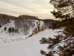 Winter landscape: view from the high bank of a frozen river to a cliff overgrown with trees