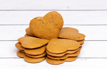 A stack of crispy cookies in the shape of hearts on a light, wooden background. Close-up.