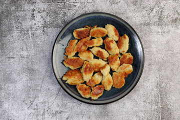 Pan-fried potato gnocchi on a round plate on a dark gray background. Top view, flat lay