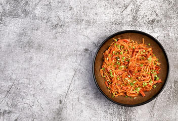 Spicy sausage noodles with green onions on a round plate on a dark gray background. Top view, flat lay