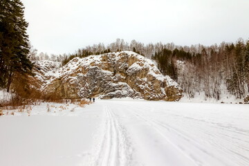 Winter landscape with a big stone, forest, sky from a frozen river