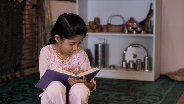 A young school-age child / kid sincerely studying for her exams - girl's education  beti bachao beti padao  future generation. Village scene of an Indian girl reading her school textbook while sitt...