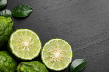 Fresh ripe bergamot fruits with green leaves on black table, flat lay. Space for text