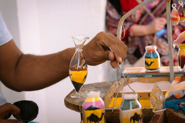 man pours multicolored sand into a glass jug. Making multicolored sand for handmade souvenirs