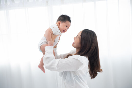 Happy family. Laughing mother lifting her adorable newborn baby son in air, copy space. asian mother lifting and playing with newborn baby, Health care family love together. Asian girl lifestyle.