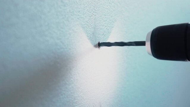Young Male handyman using power drill with light  to drill a hole in a white wall at home detail close up  4K