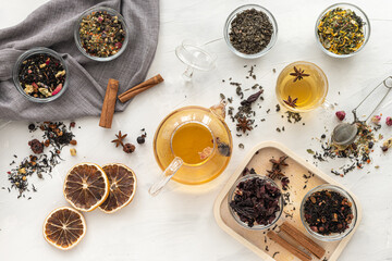 Several varieties of herbal and fruit tea in glass bowls and a kettle with a cup of hot tea on a...