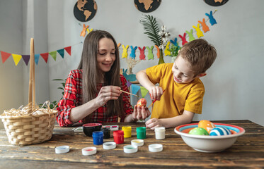 Mom and child in bright clothes together are coloring eggs in a decorated room. Concept of happy family and preparation for Easter