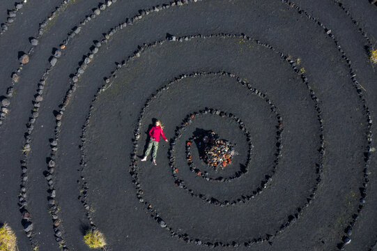 Woman motorcyclist lying on black ground ash volcanic slag. Spiral lined with stones in the zone of the Tolbachik volcano Kamchatka
