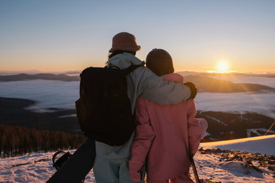 Snowboarders couple enjoying sunrise in mountains ski resort