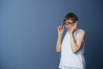 Portrait of an elderly woman on a gray-blue background carefully looking something through glasses