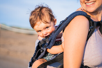 Fototapeta na wymiar Baby chewing on the strap of a baby carrier outdoors