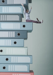 Cheerful businesswoman sitting on the top of stacked ring binders