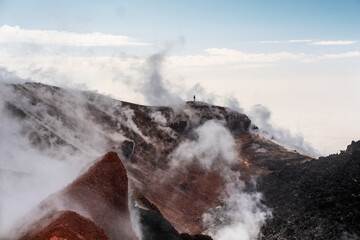 man standing on the crater of active volcano. Red earth, gas, steam