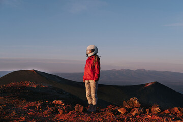 Woman wearing motorcycle helmet in volcano valley. Misted glass, red hills, a view like on another planet Martian landscape