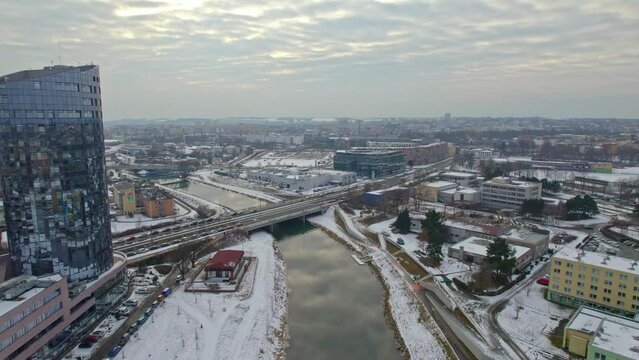 Snowy city of Olomouc, view of river with bridge and tall building with mirrored windows, cold winter panorama from drone