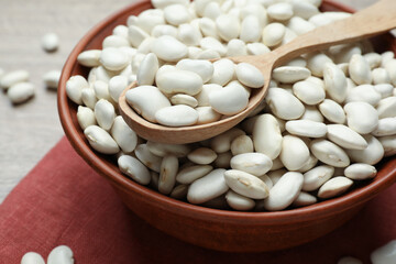 Raw white beans and spoon in bowl on table, closeup
