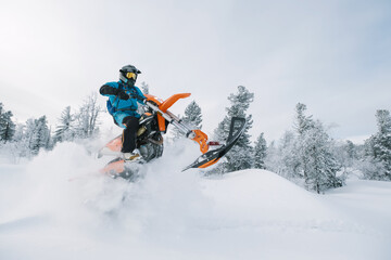 Naklejka na ściany i meble Snowbike rider in mountain valley in beautiful snow powder. Modify dirt bike with snow splashes and trail. Snowmobile sport riding, winter sunny day