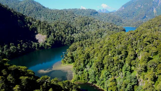 Aerial dolly in of turquoise lake between Andean mountains with dense green rain forest, Huerquehue National Park, Chile