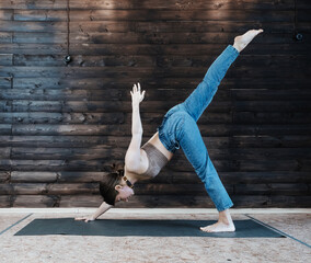 Young woman wearing jeans doing yoga at home. Eka pada adho mukha svanasana yoga pose