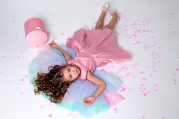 Obraz na płótnie Canvas beautiful little girl in a chic pink dress lies on the floor strewn with confetti. top view. fashion and style. child celebrates his birthday. photo in the studio. space for text. High quality photo
